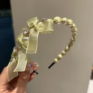 Close-up of sage green satin headband featuring pearls, bows, and sparkling rhinestones