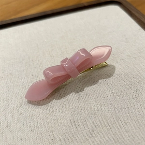 Detail of pink acetate bow hair clip with gold metal duckbill clamp on fabric