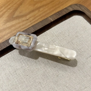 Detail of cream acetate hair clip with square resin inlay and gold metal duckbill clip