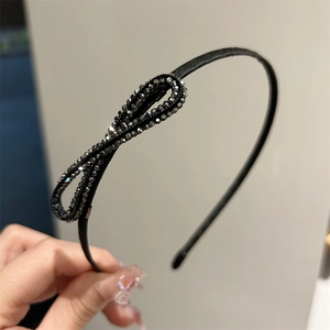 Détail d'un serre-tête noir fin orné d'un nœud latéral avec des strass brillants et élégants
