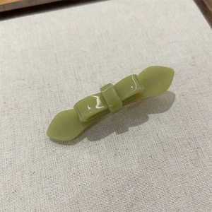 Detail view of a glossy matcha green double-layer acetate bow hair clip on linen background