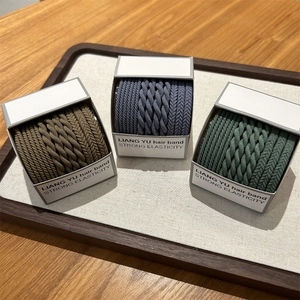 Close-up of three boxes of woven high-elastic hair ties in brown, blue-grey, and dark green