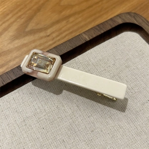 Close-up of cream acetate hair clip with amber square gemstone on a wooden display tray