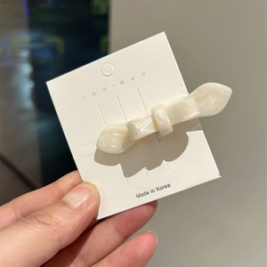Detailed macro view of white pearlescent acetate bow hair clip on a display card