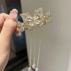 Gros plan détaillé de la pince à cheveux papillon dorée avec strass et longs pompons