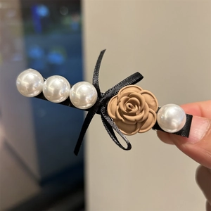 Detail view of retro rose hair clip featuring white pearls and a black ribbon bow