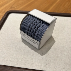 Detail of grey braided high-elasticity hair bands in a white branded display box