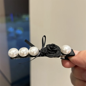 Macro detail of retro black rose hair clip with white faux pearls and satin ribbon