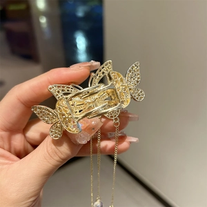 Détail d'une pince à cheveux papillon dorée avec de longues chaînes à pompons et perles