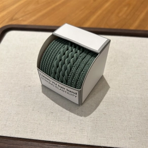 Detail of dark green woven elastic hair bands on a textured tray in minimalist style