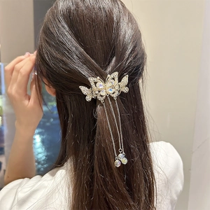 Détail d'une pince à cheveux papillon dorée avec glands et strass sur une demi-queue