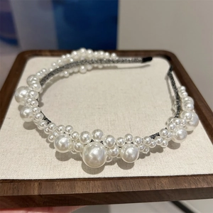 Detail shot of elegant white pearls layered on a slim headband over wooden tray