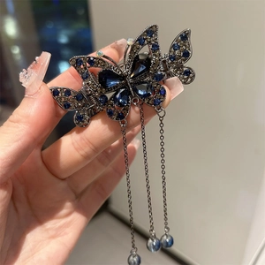 Détail d'une pince à cheveux papillon avec strass bleus et de longs glands en métal