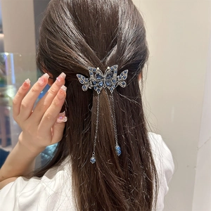 Détail de la pince à cheveux papillon argentée avec cristaux bleus et pompons en métal