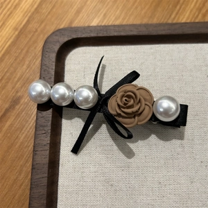 Detail view of a vintage resin rose hair clip with white pearls and a black ribbon bow