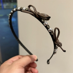 Elegant thin brown headband with rhinestone bows, shown in a close-up handheld view