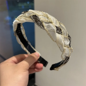 Dettaglio della fascia intrecciata color crema con ricamo in filo d'oro e strass neri