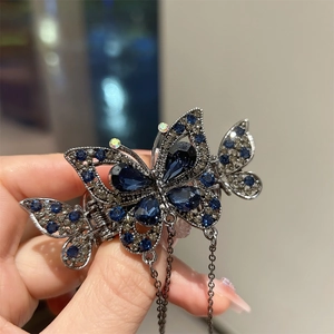 Détail de pince à cheveux papillon argentée avec cristaux bleus et chaîne à pampilles