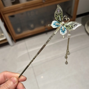 Detailed macro of golden butterfly hair pin with blue enamel and long beaded tassels