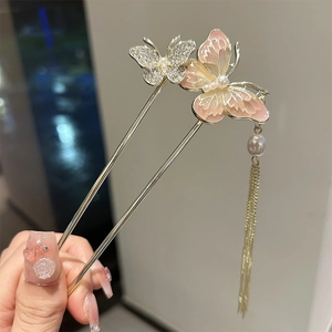 Detailed close-up of butterfly hair pin with pink enamel wings and golden tassels