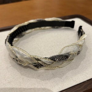 Dettaglio di un cerchietto in organza intrecciata champagne con accenti di strass scintillanti