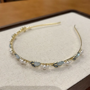 Dettaglio di un cerchietto dorato con perle, pietre occhio di gatto e cristalli blu