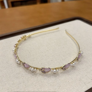 Dettaglio di un cerchietto dorato con pietre rosa e perle bianche su espositore in tessuto