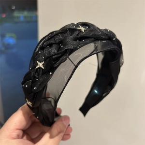 Dettaglio del cerchietto intrecciato in rete nera con stelle dorate e accenti di strass