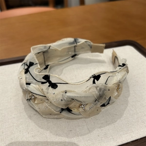 Dettaglio cerchietto a treccia in mesh crema con motivi a fiocco nero e stelle oro