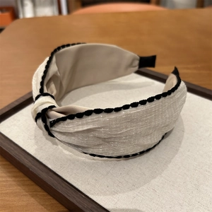 Detail shot of a white knotted headband with black wavy trim on a wooden display
