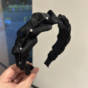 Dettaglio di un cerchietto intrecciato nero con trama a rete ed eleganti perle bianche
