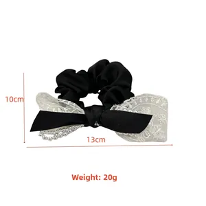 Détail du chouchou en satin noir avec nœud en dentelle blanche et chaîne de perles 13x10cm