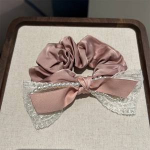 Chouchou élégant en satin rose avec nœud en dentelle et perles sur plateau beige