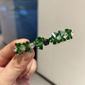 Dettaglio ravvicinato di un fermaglio vintage con cristalli verde smeraldo e base dorata