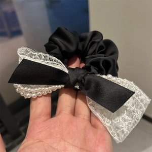 Détail du chouchou en satin avec nœud noir, dentelle blanche et bordure en perles