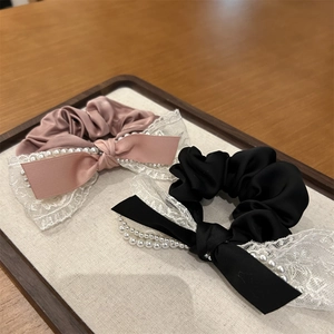 Détail de chouchous en satin avec dentelle, doubles nœuds et perles sur plateau en bois