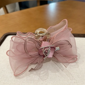 Détail d'une pince à cheveux avec nœud en maille rose, rose en satin et strass