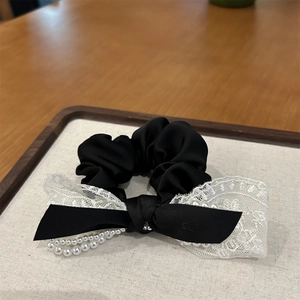 Détail de chouchou en satin noir avec nœud en dentelle blanche et chaînes de perles élégantes
