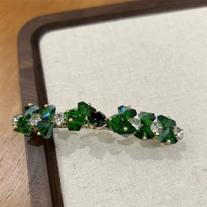 Dettaglio di un fermaglio per capelli dorato con cristalli verde scuro e trasparenti