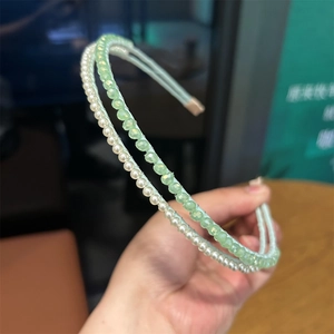 Detailed view of pearl and green crystal beaded headbands held by hand for display