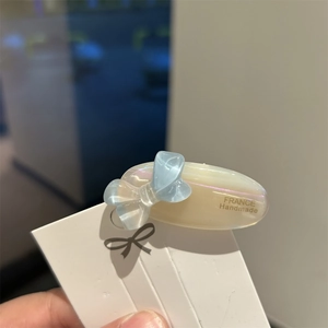 Detail of a pearlescent oval hair clip featuring a light blue bow and handmade engraving
