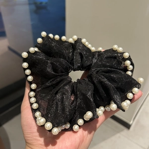 Détail d'un chouchou en maille noire avec tissu scintillant et perles cousues