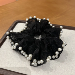 Détail macro du chouchou en maille noire avec perles blanches pour coiffure élégante