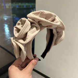 Detail of a beige wide headband featuring three large handcrafted fabric roses in retro style