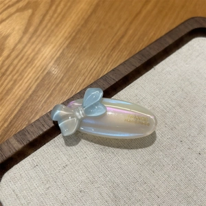 Detailed macro of a pearlescent acetate hair clip with a blue bow and handmade gold text