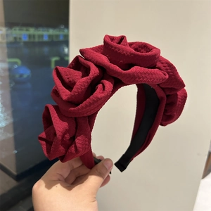 Detail of dark red handcrafted oversized fabric roses on a textured wide headband
