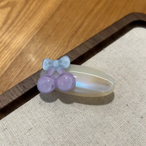 Detail of handmade oval acetate hair clip with blue bow and purple bead on cream base
