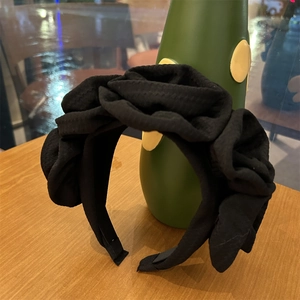 Detail of the oversized pleated rose ornament and textured black fabric on the headband