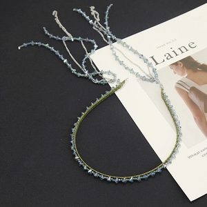 Detail of beaded headband with gradient crystal tassels and silver chains on black surface