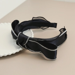 Dettaglio cerchietto in raso nero con fiocco e bordi di strass su un piatto bianco decorato